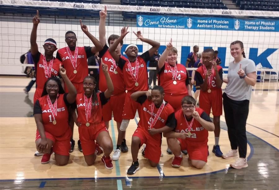  A basketball team in red uniforms celebrates with medals on a court.